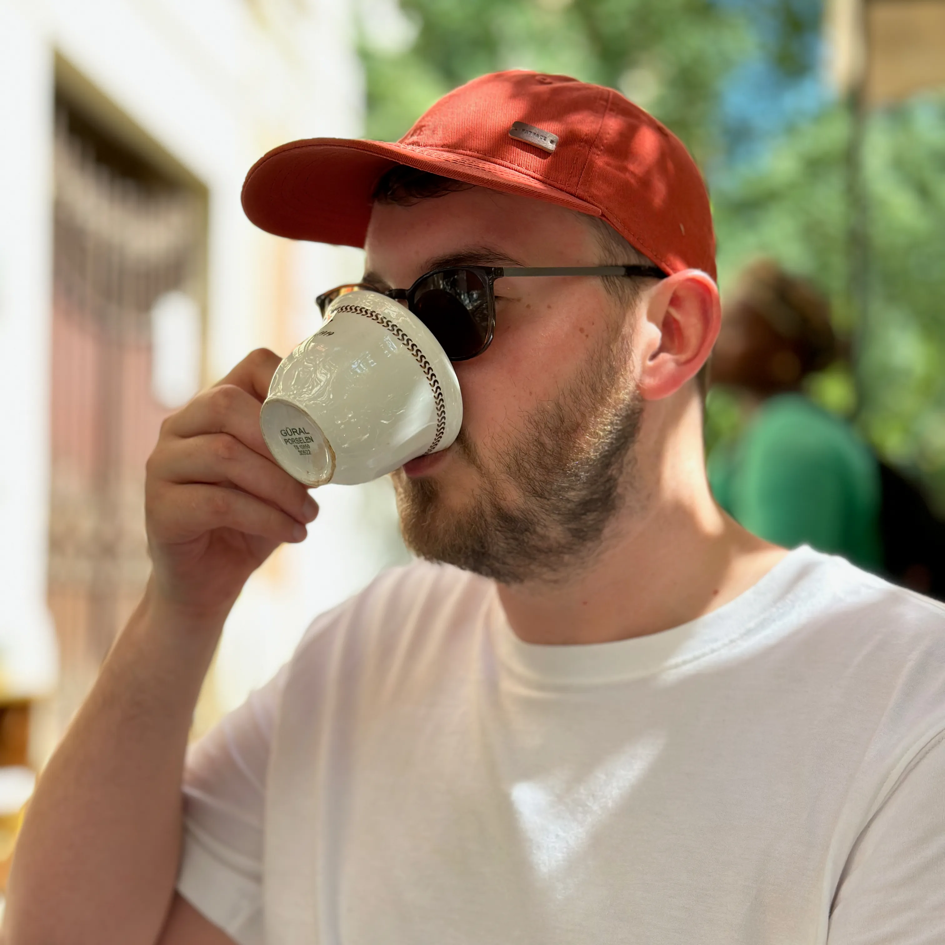 An image of Alex Kearns, drinking an espresso wearing a baseball cap.